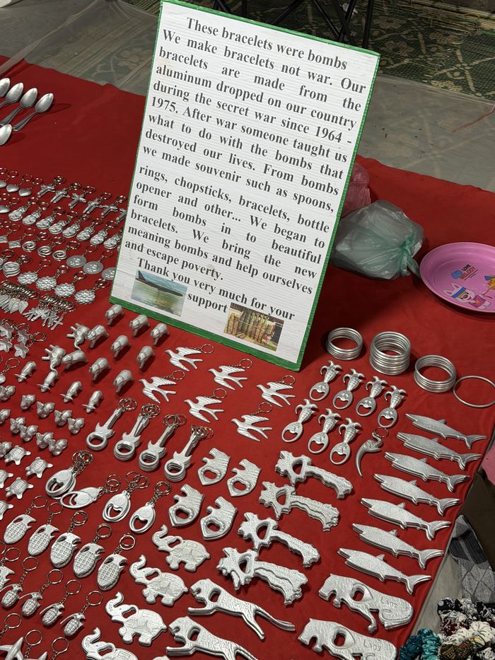 Bracelets and spoons for sale next to a sign explaining they are made from bombs