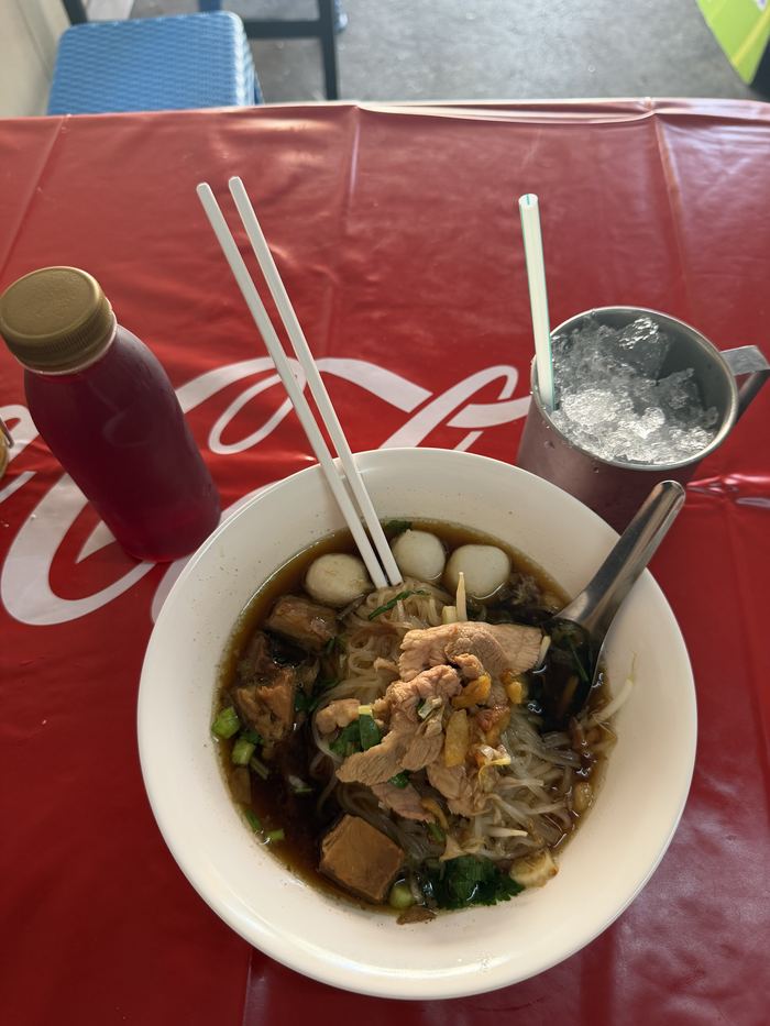 A bowl of noodle soup with meatballs on a red table