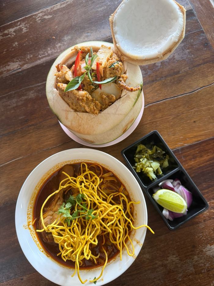 A bowl of khao soi next to a curry served in a coconut