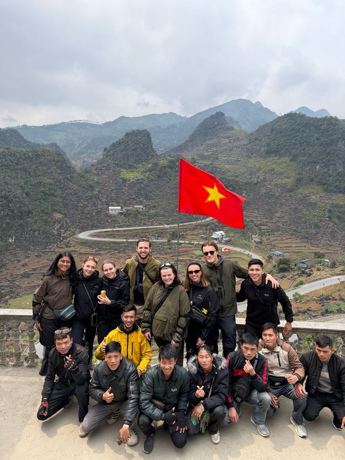 The tour group posing with a Vietnamese flag and mountains behind them