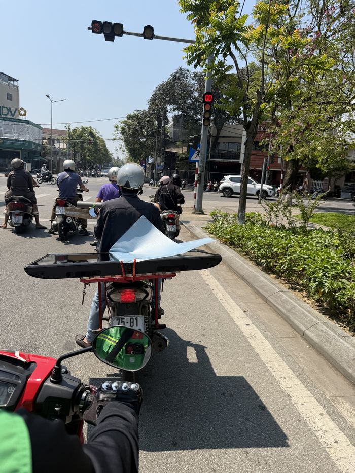 Riding behind a motorbike that is carrying a TV