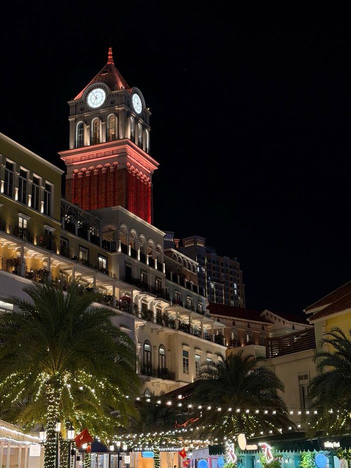 A red clock tower and lit-up buildings at night
