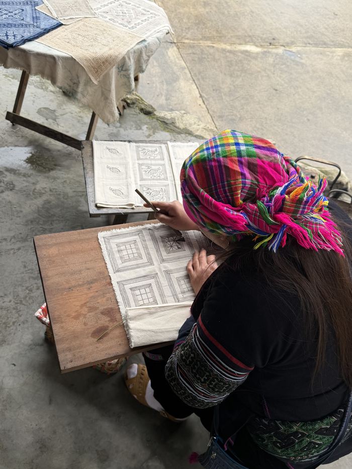 A woman in a bright headscarf drawing a batik pattern on cloth
