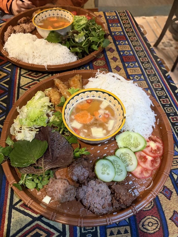 Bun cha with grilled pork, noodles, and herbs on a woven tray