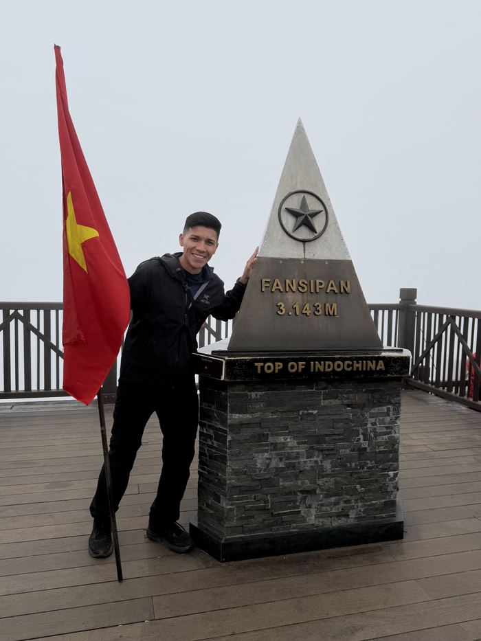 Standing by the Fansipan summit marker with a Vietnamese flag